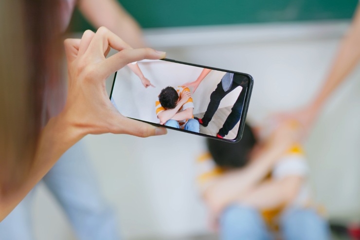 Ragazzi che filmano un ragazzino che piange seduto per terra. Cyberbullismo