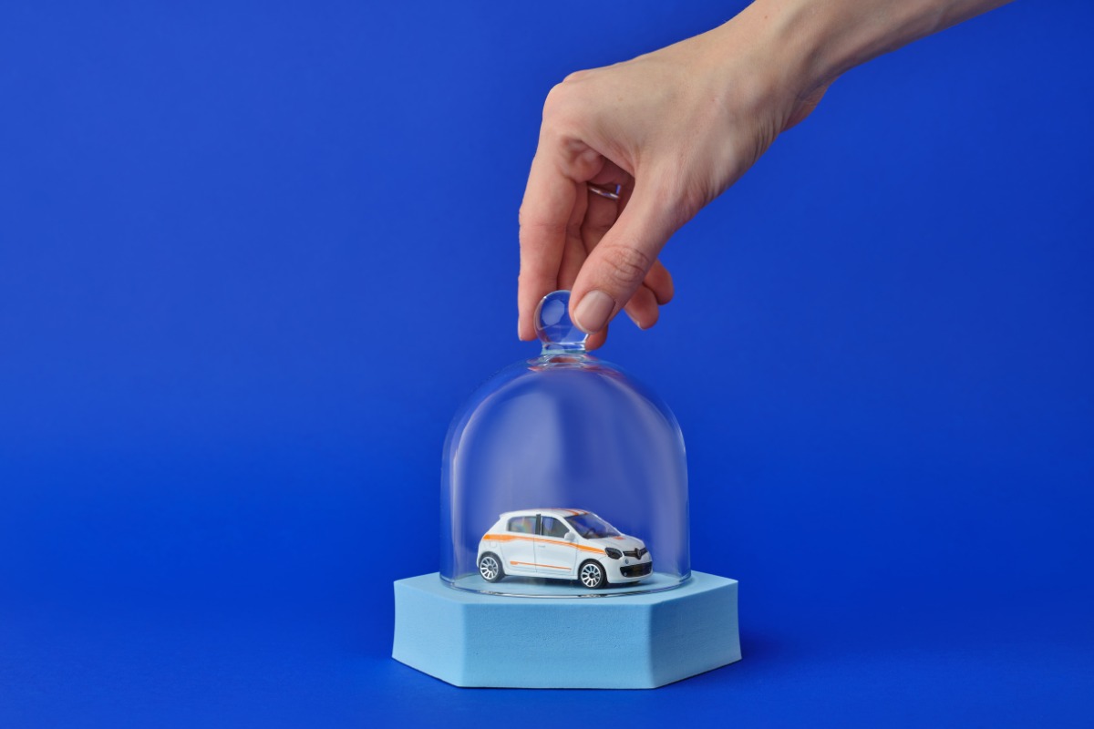 Auto giocattolo dentro ad una bolla di vetro su sfondo blu: concetto di assicurazione