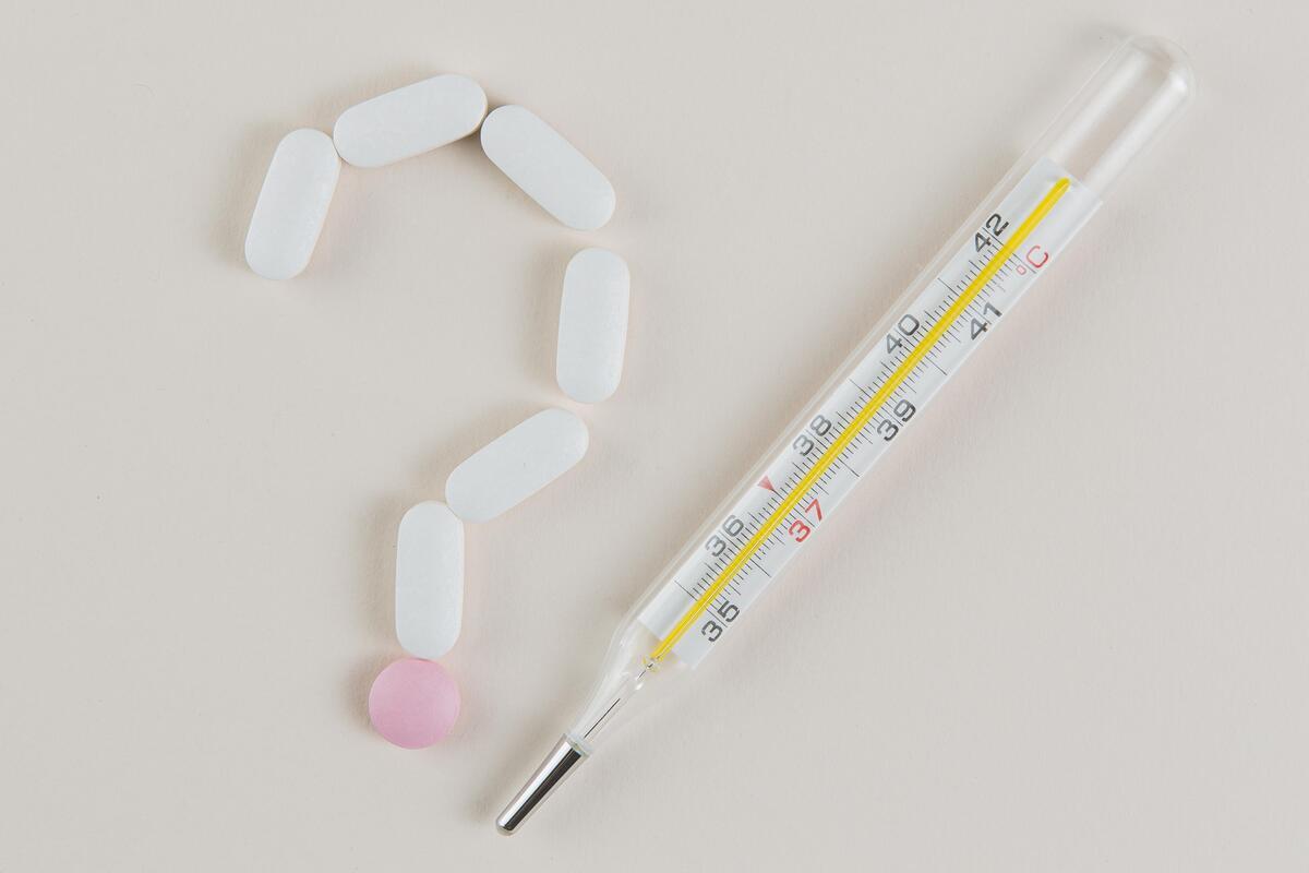 Pillole disposte a punto di domanda e termometro